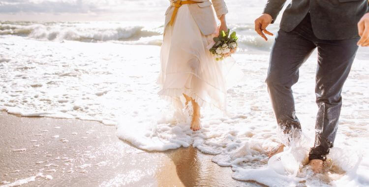 A newlywed couple standing in the water on a beach.